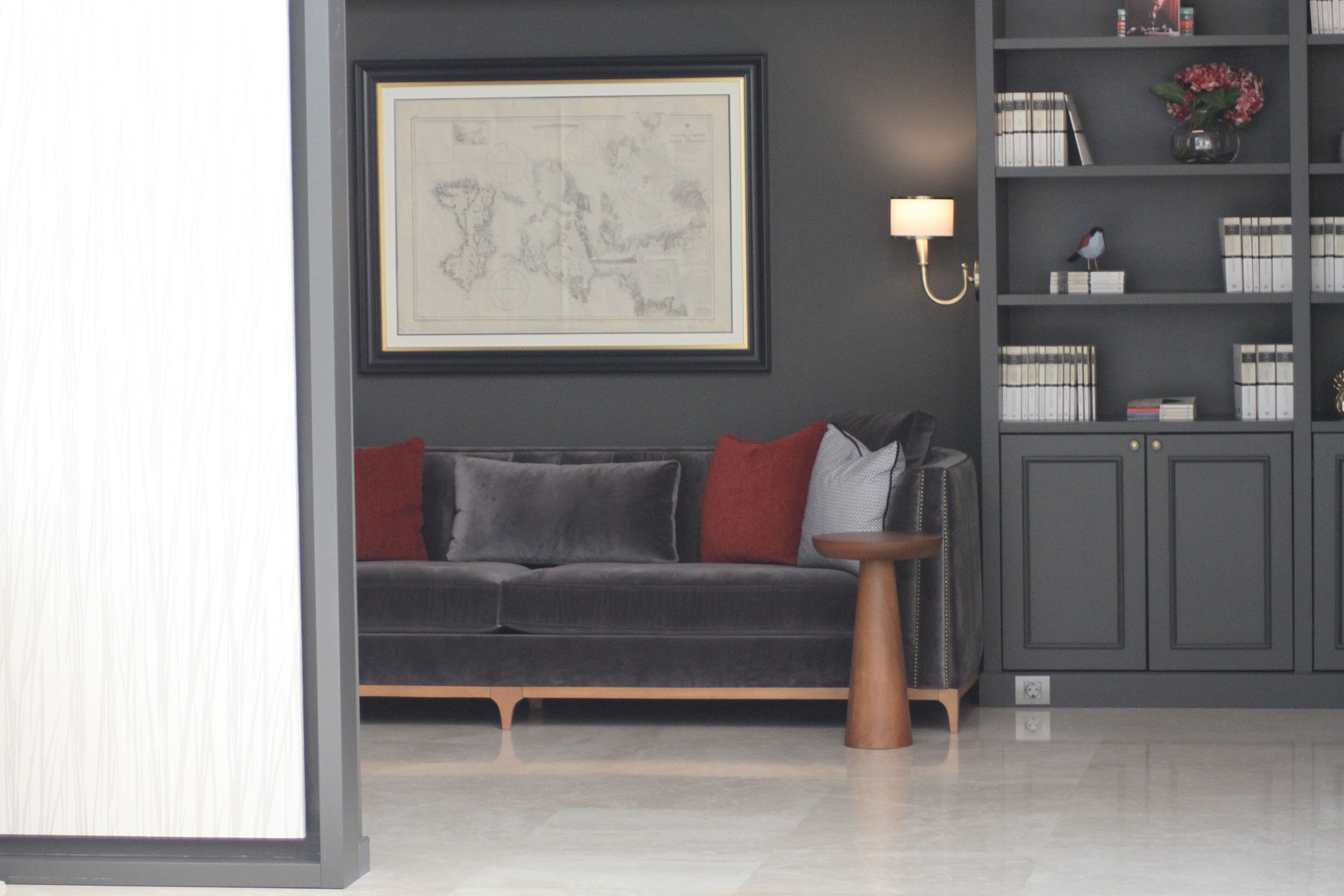 Una sala de estar moderna con un sofá gris, cojines rojos, una mesita de madera y una estantería con libros y objetos decorativos.