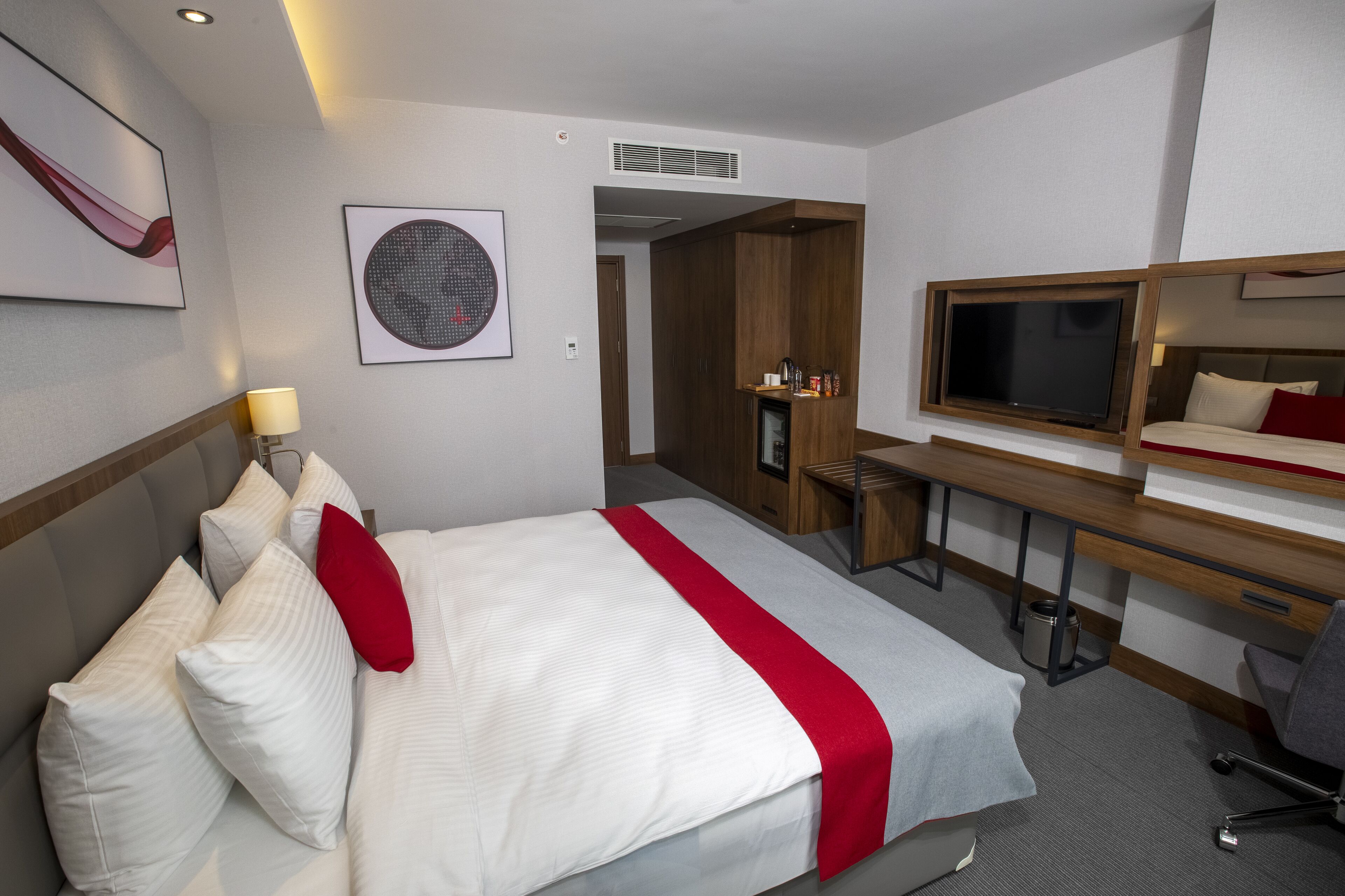 A hotel room with a bed, desk, chair, TV, and artwork on the walls.