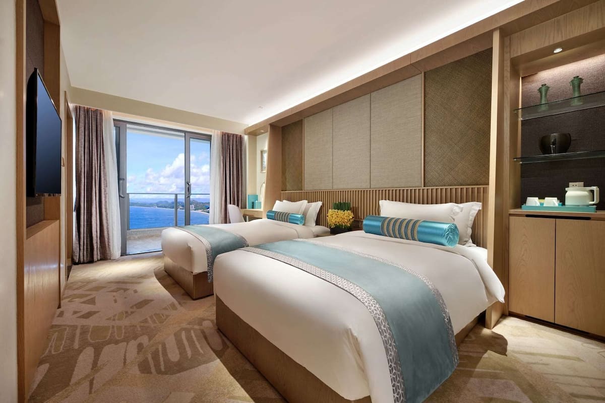 A hotel room with a large bed, a TV, a balcony with a view, and a minibar.