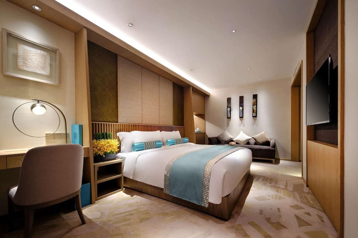 A modern hotel room with a large bed, a desk, a chair, and a television.