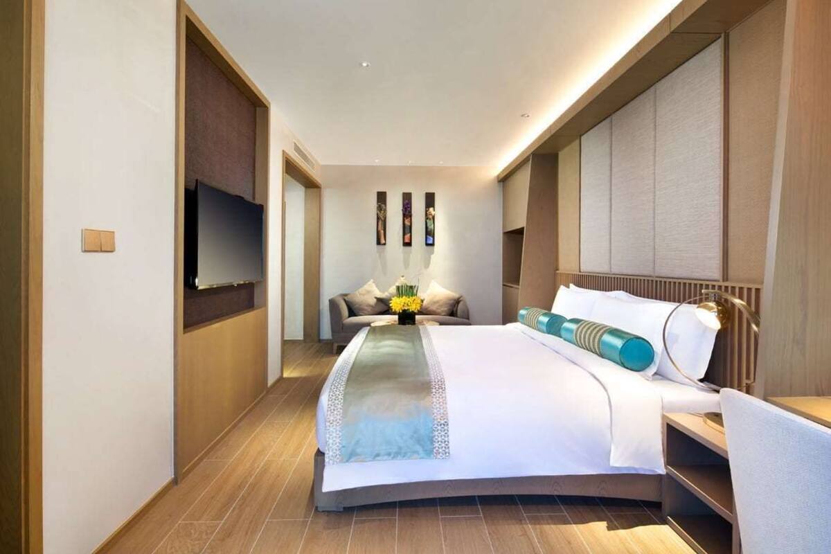 A modern hotel room with a large bed, a TV mounted on the wall, and a small seating area with a table and chair.