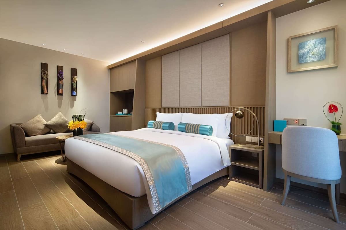 A modern hotel room with a large bed, a sofa, a desk, and a chair.