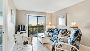 A living room with a sofa, two chairs, a TV, and a table. There is a balcony with a view of the sea. - 3228 Ocean Front 2nd Floor (St. Augustine)