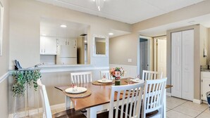A dining area with a wooden table, white chairs, a small plant, and a mirror above the table. - 3228 Ocean Front 2nd Floor (St. Augustine)