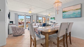 A spacious dining area with a wooden table, four upholstered chairs, and a chandelier. - Renovated Coastal Escape with Balcony Overlooking the Ocean (St. Augustine)