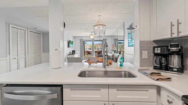 A modern kitchen with a stainless steel sink, white cabinetry, a coffee maker, and a chandelier. - Renovated Coastal Escape with Balcony Overlooking the Ocean (St. Augustine)