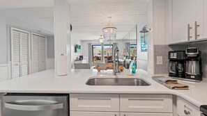 A modern kitchen with a stainless steel sink, white cabinetry, a coffee maker, and a chandelier.