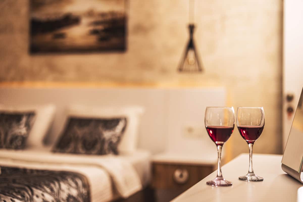 Un dormitorio con una cama, dos mesitas de noche y dos copas de vino sobre una de ellas.