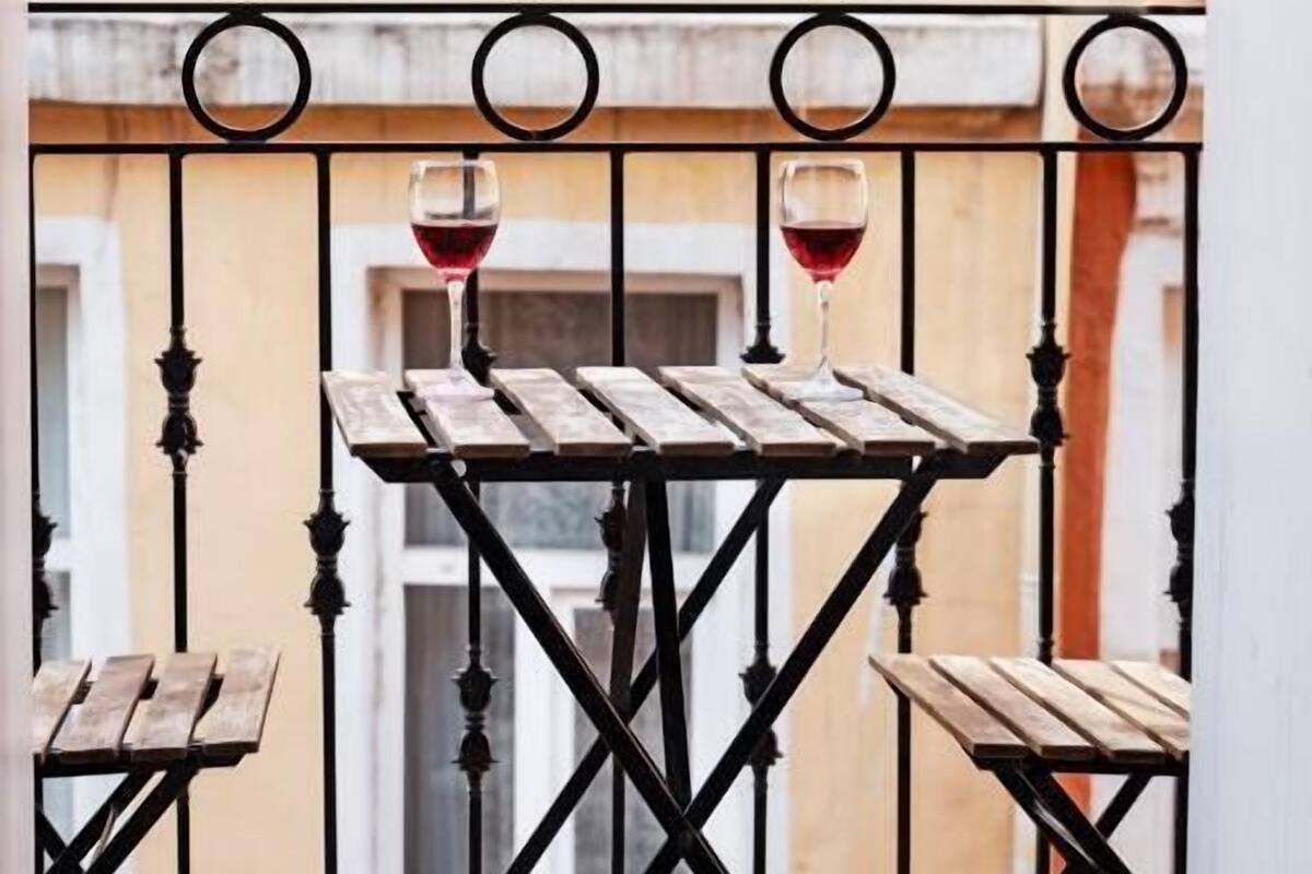 Un balcón con una mesa de madera y dos bancos, cada uno con una copa de vino tinto.