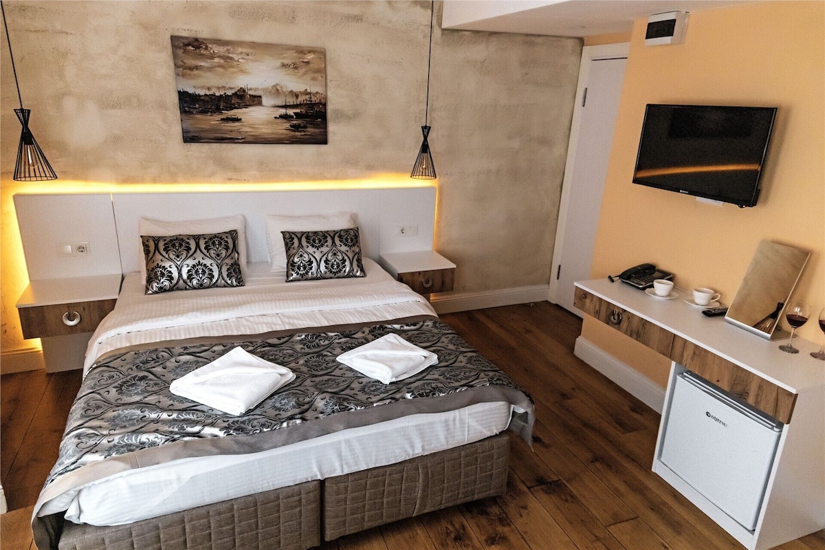 Un dormitorio con cama, mesitas de noche, televisión, escritorio con teléfono y un refrigerador pequeño.