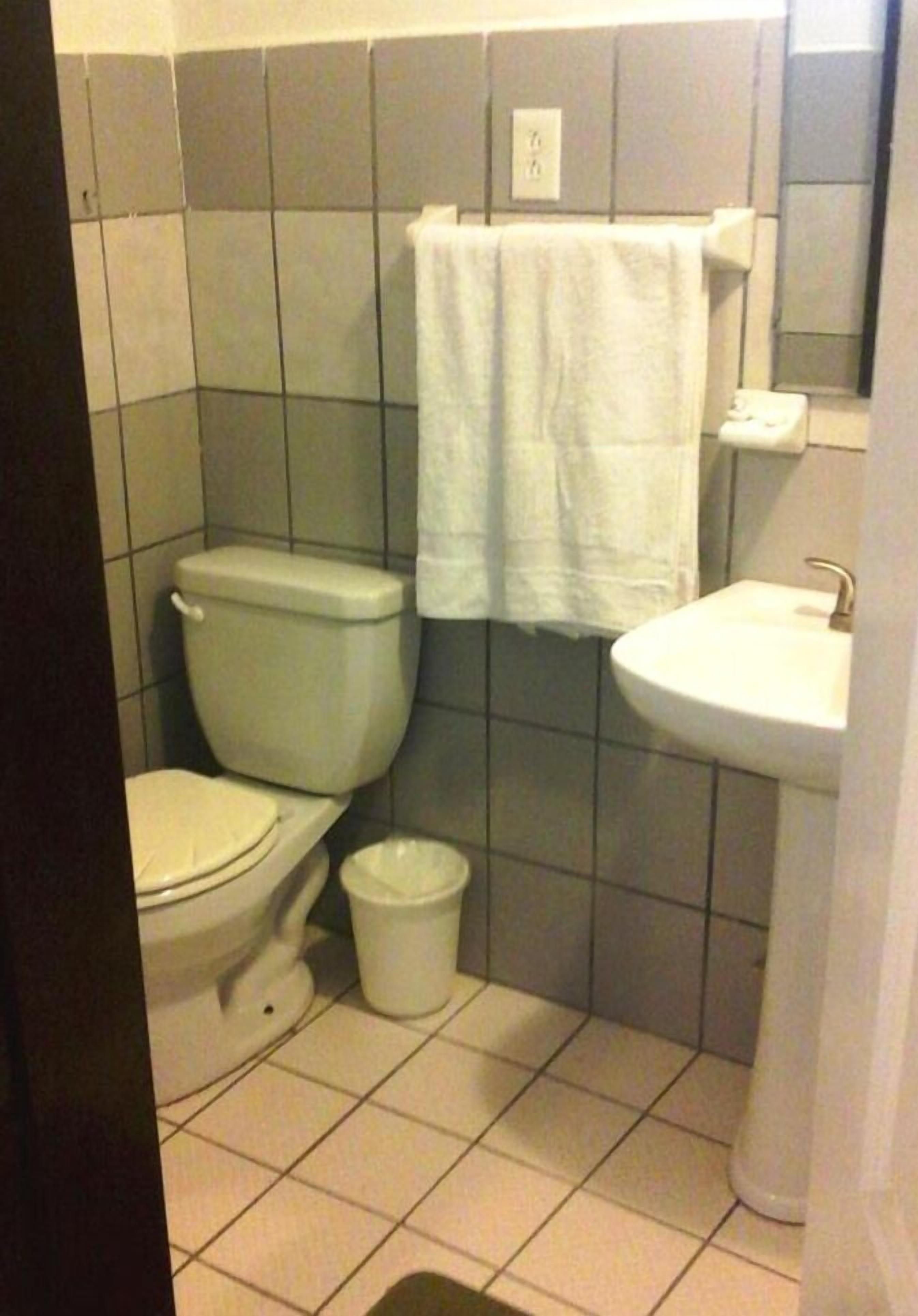 A small bathroom with a toilet, sink, and a white trash bin.