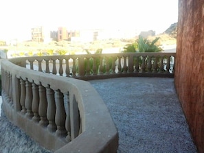 A curved balcony with a balustrade, a concrete floor, and a view of buildings and palm trees in the background. - Hotel Whale Hill By Rotamundos (Puerto Peñasco)