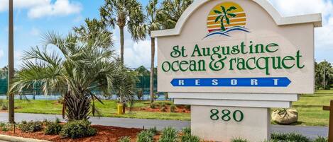 A sign for St. Augustine Ocean & Racquet Resort with a palm tree and a view of the water.