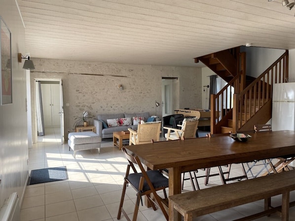Amplia sala de estar con una mesa de comedor de madera, sillas acolchadas, un sofá y una escalera que conduce a un nivel superior.