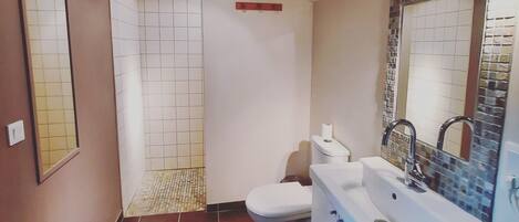 Et badeværelse med toilet, håndvask og bruseområde.