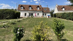 Ein zweistöckiges Haus mit geneigtem Dach, einer Veranda und einem kleinen Garten mit Blumen und Sträuchern.