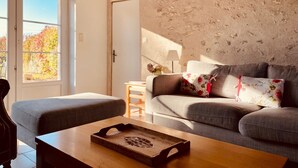 Ein Wohnzimmer mit einer Couch, einem Holztisch und einer Tür zu einem Balkon mit Herbstlaub.
