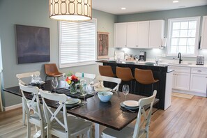 A dining area with a dark wooden table, white chairs, and a kitchen in the background.