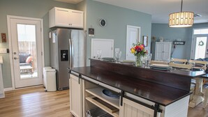 A kitchen with a central island, white cabinetry, a stainless steel refrigerator, and a dining area with a table and chairs. - NEW 3 BR/2.5BTH near Bethany Beach/home on stilts, open floor plan/1st FL Master (Ocean View)