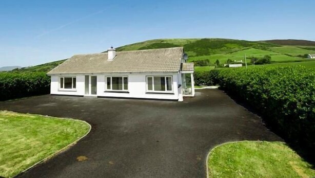 A white two-story house with a tiled roof, surrounded by green fields and hills. - Great renovated house in the village of Louisburgh (Louisburgh)