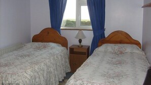 Une chambre avec deux lits simples, une table de chevet avec une lampe et une fenêtre avec des rideaux bleus.
