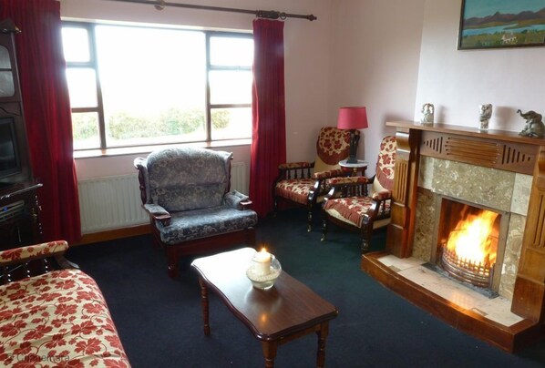 Een gezellige woonkamer met een open haard, een bank, een fauteuil en een tafel met een kaars.
