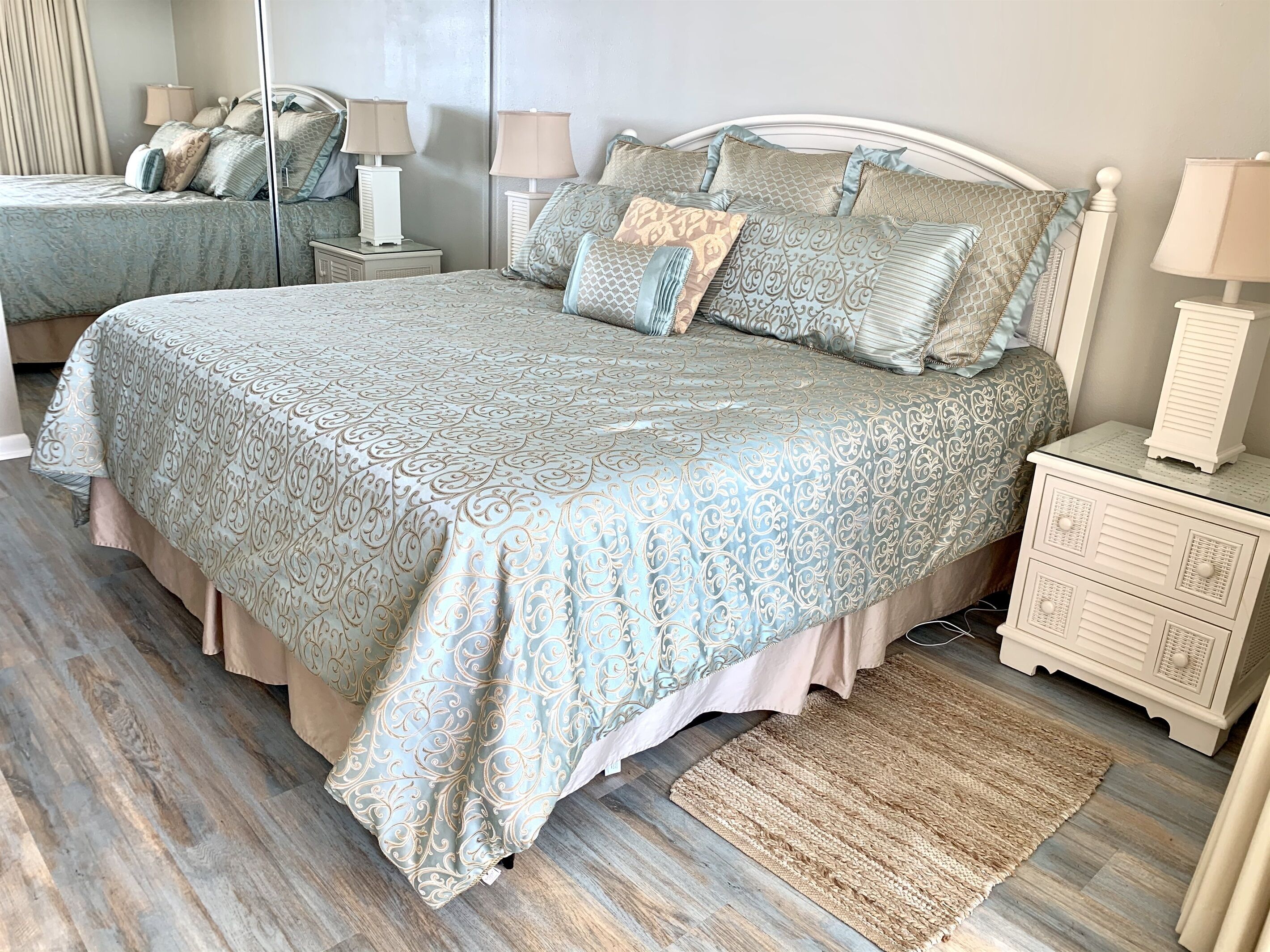 A bedroom with a large bed, two bedside tables, a mirror, and a rug.