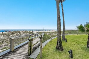 Une promenade en bois qui mène à une plage bordée de palmiers et d’où l’on a une vue dégagée sur l’océan.