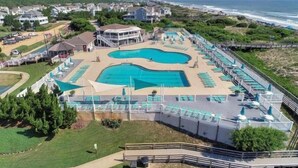 A resort with a large pool, beach chairs, and a view of the ocean.