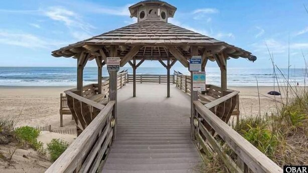 A wooden beach gazebo with a covered walkway leading to it.