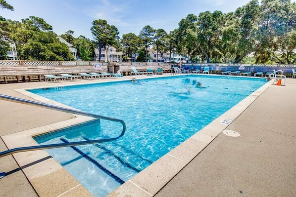 A swimming pool with clear blue water, surrounded by a wooden deck and a fence.