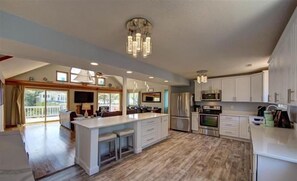 A spacious kitchen with a large island, modern appliances, and a chandelier. - LilyBeth | 7BR Corolla Light Resort · Private Pool · Sleeps 17 (Corolla)