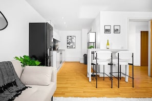 A modern living room with a sofa, a dining area with a table and chairs, a kitchen area, and a white door. - Birmingham City Centre - Twin Beds - Smart TV
 (West Midlands)