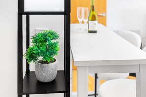 Un espace repas moderne avec une table blanche, une plante en pot et une bouteille de vin posée sur une étagère.