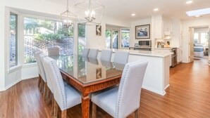 Una cocina moderna con una mesa de comedor de vidrio, armarios blancos y vista al jardín trasero.