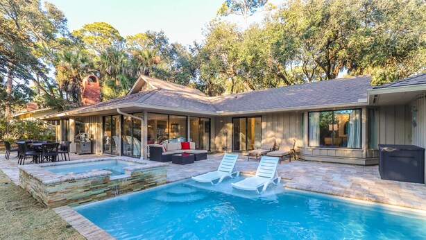 Una casa moderna con piscina, mobiliario de exterior y un patio cubierto.