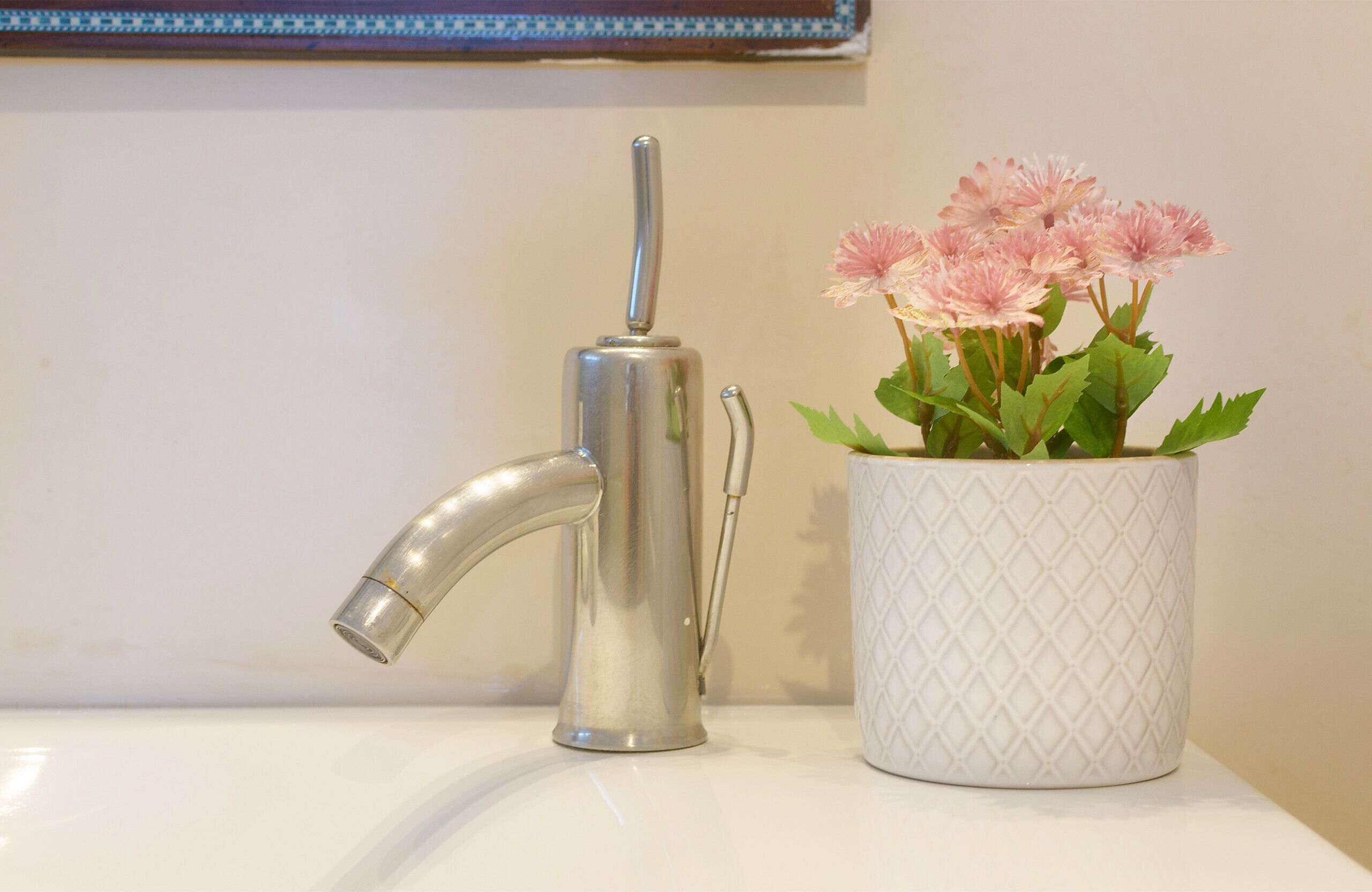 Un lavamanos de baño con un grifo moderno y una jarra blanca decorativa con flores rosadas.