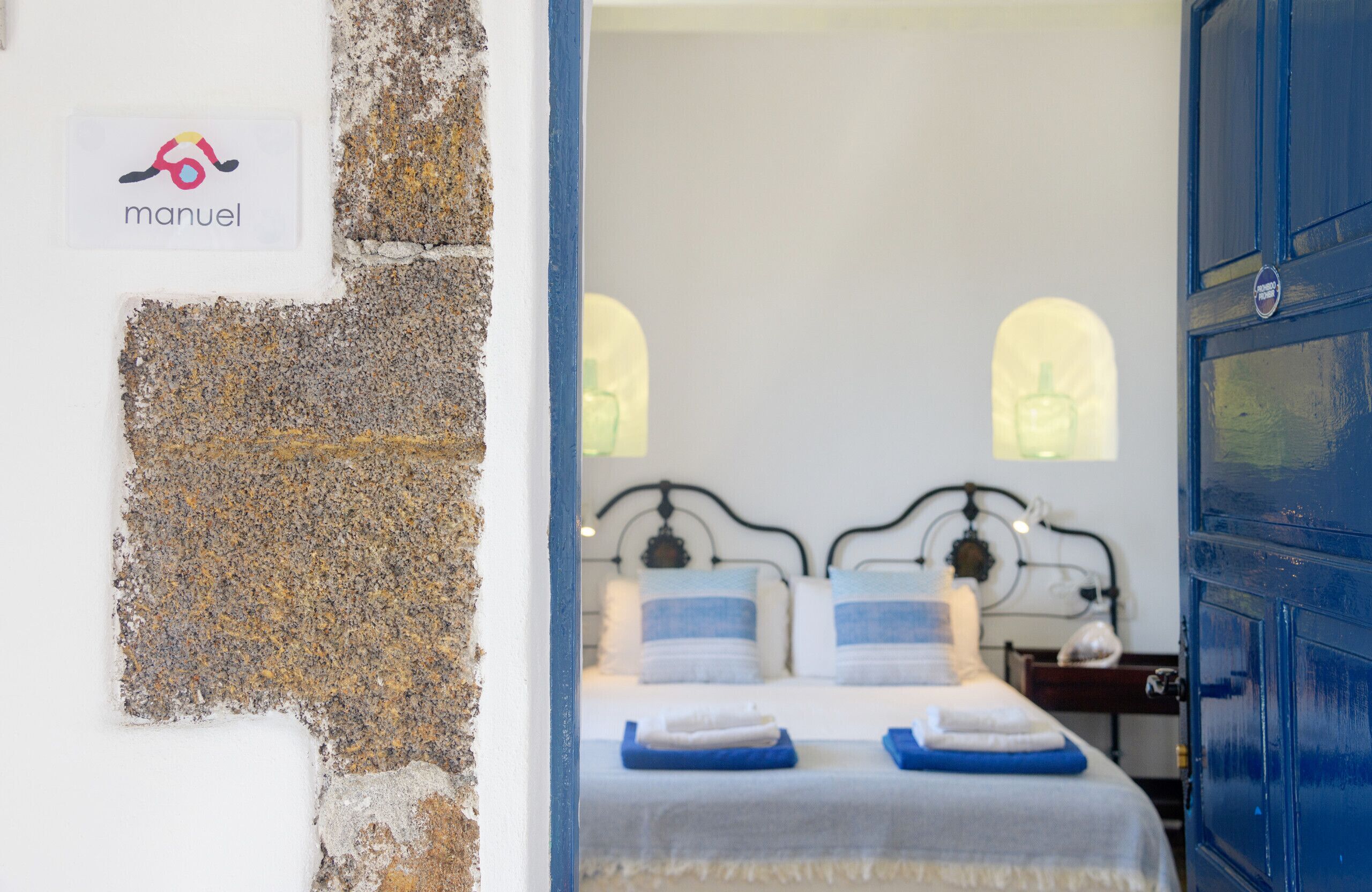 A hotel room with a bed, a nightstand, and a blue door.