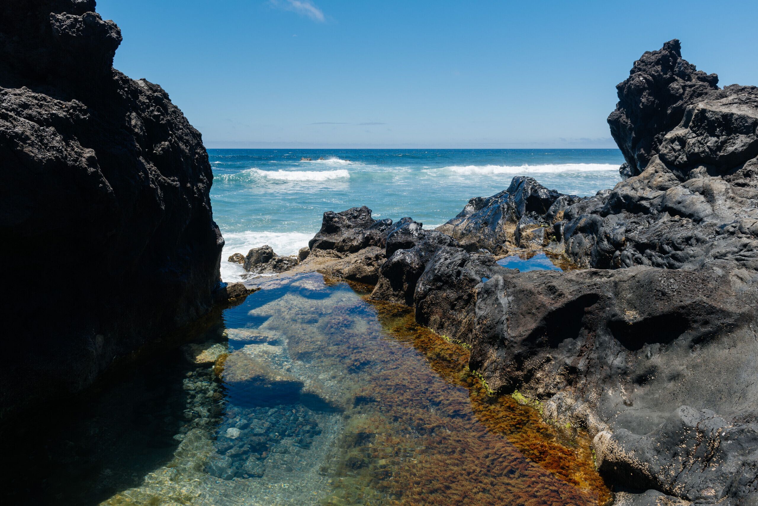 Une côte rocheuse aux eaux limpides, où les vagues se brisent.