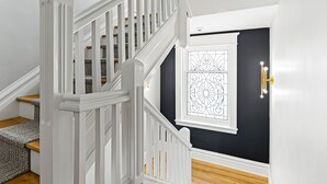 Una escala amb baranes blanques i una porta negra amb un panell de vidre decoratiu.