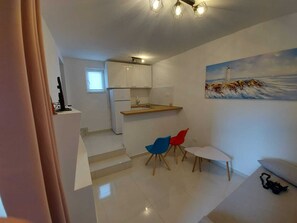 A compact kitchen with white cabinets, a small dining area with two chairs, and a painting of a lighthouse on the wall. - Ferienwohnung (Pakoštane)