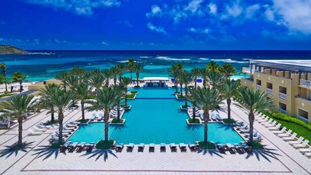 Una piscina di un resort con vista sull'oceano, circondata da palme e lettini.