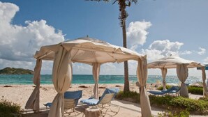Una spiaggia con due zone relax coperte, ciascuna con un ombrellone e poltrone prendisole.