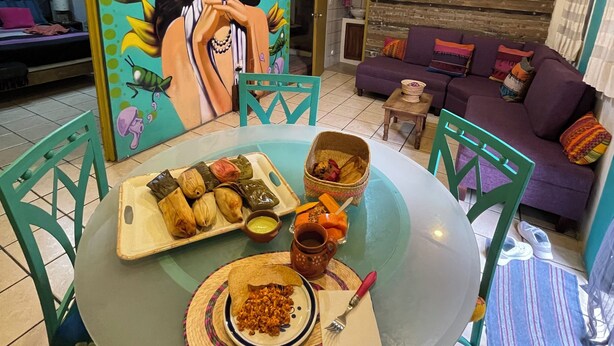 Un coin repas avec une table ronde en verre, des chaises colorées et une fresque murale.