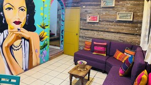 Un salon animé, agrémenté d’une fresque colorée, d’un canapé violet et d’un mur en bois orné de tableaux encadrés.