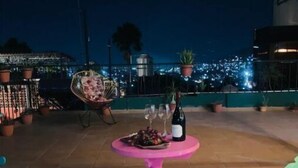 Un espace extérieur aménagé en terrasse, avec une table rose dressée pour un repas, entourée de chaises et de plantes en pot.