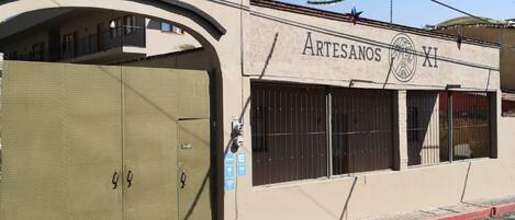 A building with a closed metal gate, a sign reading 'ARTESANOS XI', and a clear blue sky.