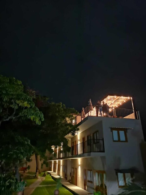 Un edificio de varios pisos con balcón, rodeado de follaje.