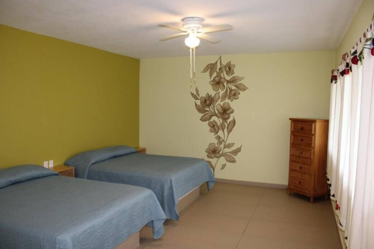 A room with two beds, a ceiling fan, a floral wall decal, and a wooden dresser.