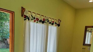 Una habitación con ventana cubierta por un cortinón floral, un lavamanos con espejo y suelo de baldosas.